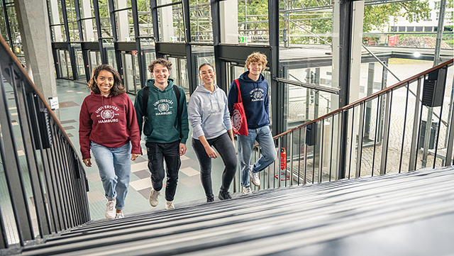 Uni_HH_10-2021-2497-640 Vier Studierende gehen nebeneinander eine Treppe hoch, im Eingangsbereich des Audimax. Das Foto ist von oben an der Treppe aufgenommen.